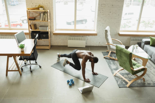 Home-workout-man-exercising-on-a-yoga-mat-while-following-a-fitness-video-on-a-laptop
