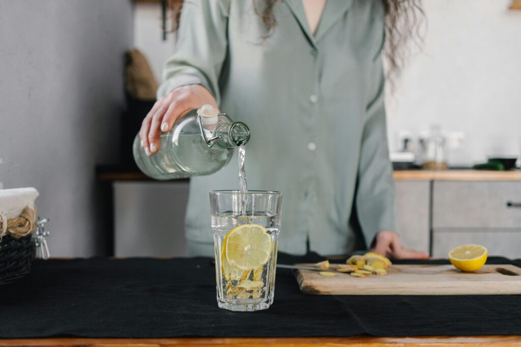 Person-pouring-water-with-lemon-into-a-glass-on-a-kitchen-counter-preparing-a-refreshing-morning-drink